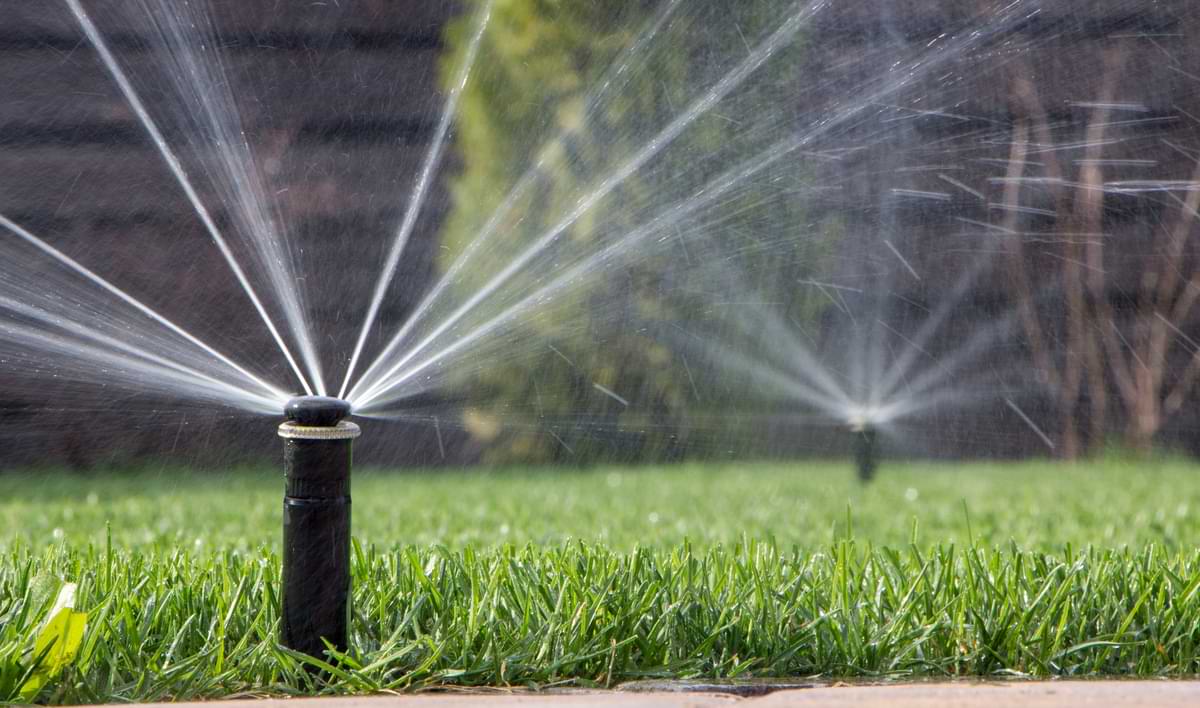 The Different Types and Uses of Sprays, Rotors, and Impact Sprinklers 1 Fixed sprinkler heads watering green grass.