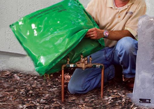 This is a picture of a man putting an insulated pouch over a backflow device outside before a freeze.