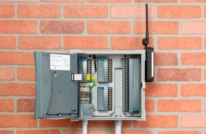 This picture has a commercial grade irrigation controller mounted on a brick wall.