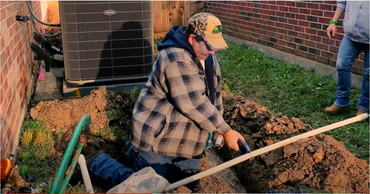an image of a professional using pipe cutters to cut pvc while he is kneeling on the dirt with an ac unit in the back.