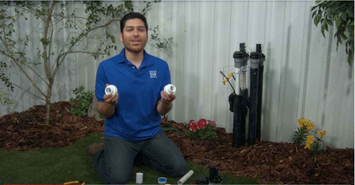 An image of the sprinklerware house pro holding two fittings outside while sitting on the grass as he demonstrates a repair.