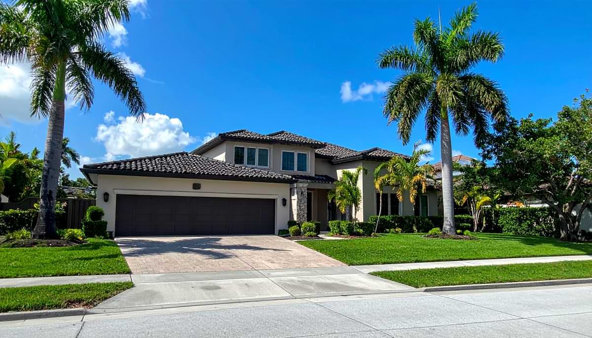 How to Winterize Palm Trees 1 Front of two-story house with Italian roofing and palm trees, both large and small, adorning the yard on a sunny day.