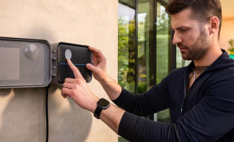 Man programming a black Rachio WiFi irrigation controller mounted against a home exterior.