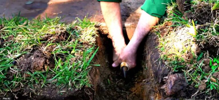 Person using both hands to grip a pvc pipe with a sidewalk sleever running through in the process of digging a trench under concrete.