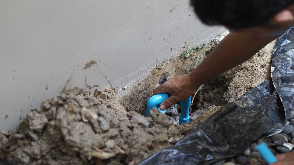 Maintenance 7 Person adjusting a blue water line under the foundation of a house.