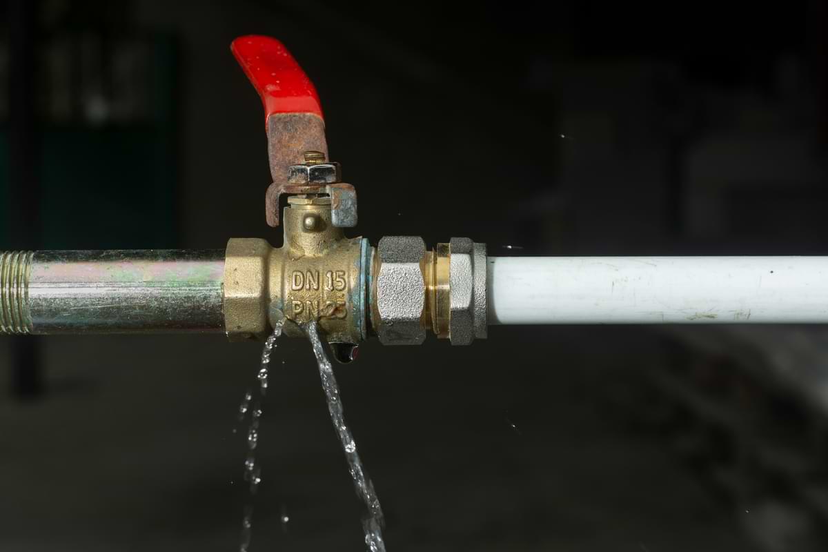 How to Fix Standing Water in Your Yard 2 Water leaking from brass backflow valve connecting a backflow device to white pvc pipe.