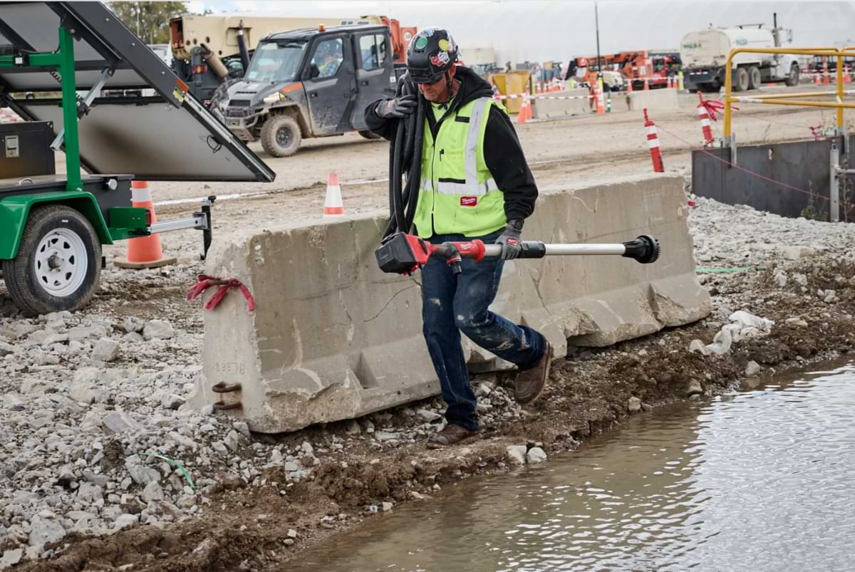 M12™ Milwaukee Stick Pumps: On-the-Go Water Removal 13 Roadside construction worker walking through mud and water on a jobsite holding a Milwaukee Tool stick transfer pump.