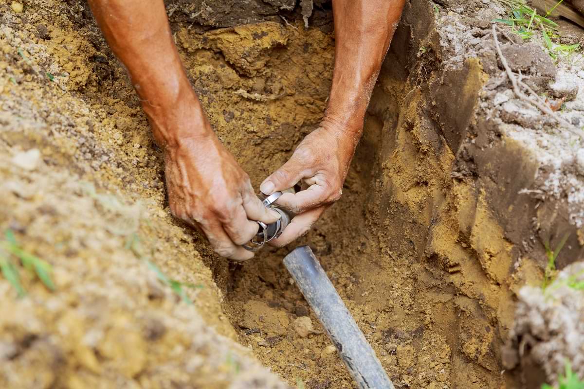 Man inspecting irrigation line connection after digging a trench. 