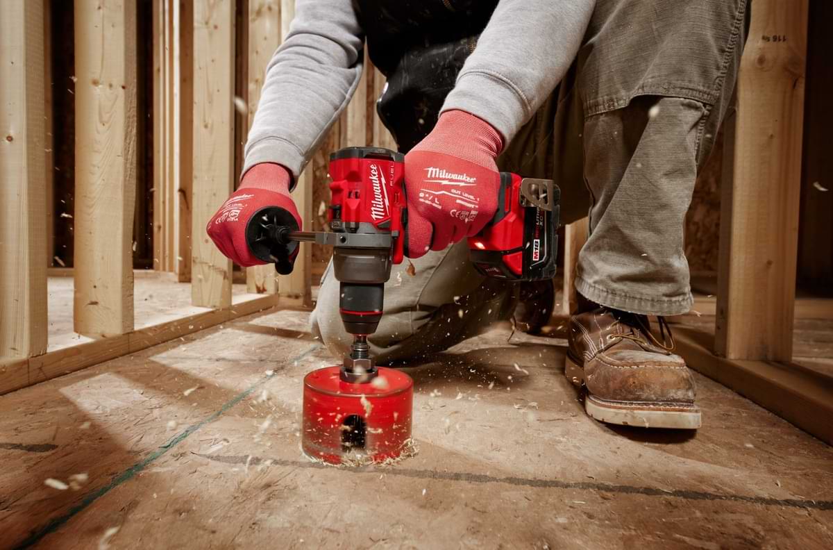 Person using Milwaukee Tool driver to drill through plywood with a construction scene backdrop.